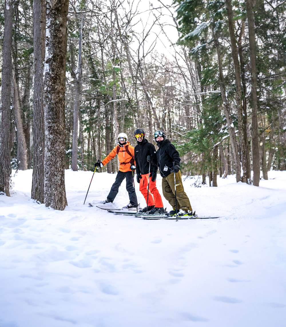 Three friends on a ski trip take a break as they emerge from the woods — Mont Rigaud, ski resort, snowboarding, alpine touring, mountain biking, and hiking, family-friendly, in Rigaud, Quebec, near Montreal