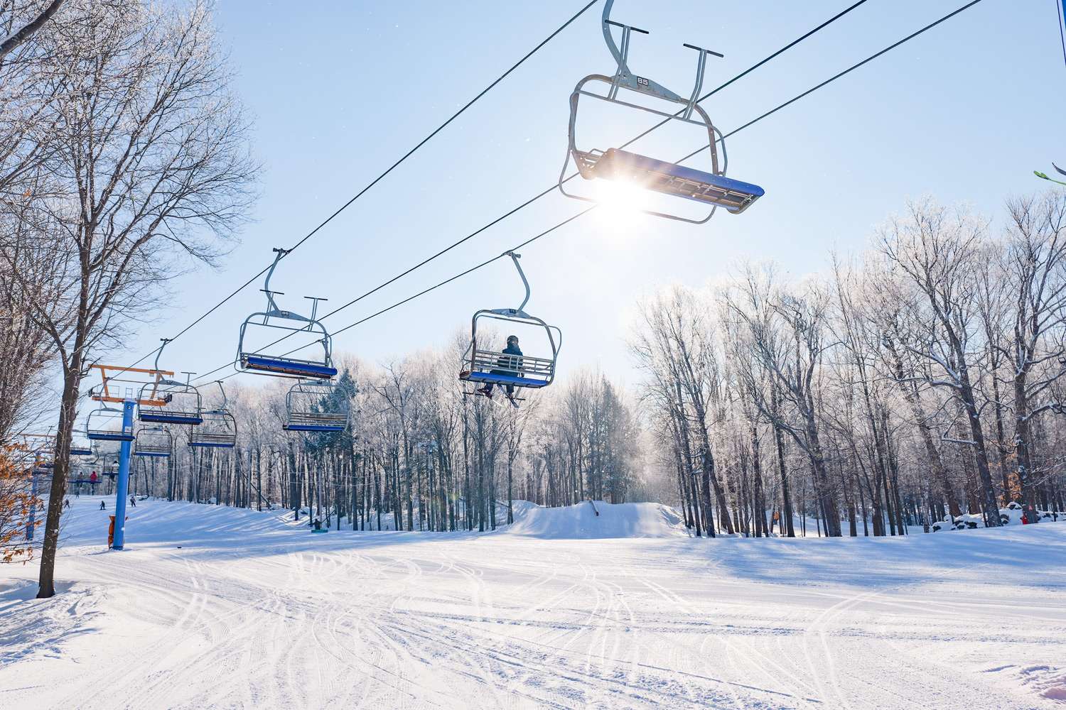 A person on a ski lift on a sunny, snowy day — Mont Rigaud, ski resort, snowboarding, alpine skiing, mountain biking, and hiking, family-friendly, in Rigaud, Quebec, near Montreal