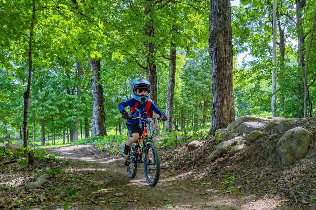 Un jeune en vélo de montagne dans un sentier boisé — Mont Rigaud, station de ski, planche à neige, randonnée alpine, vélo de montagne et randonnée pédestre, familiale, à Rigaud Québec, près de Montréal